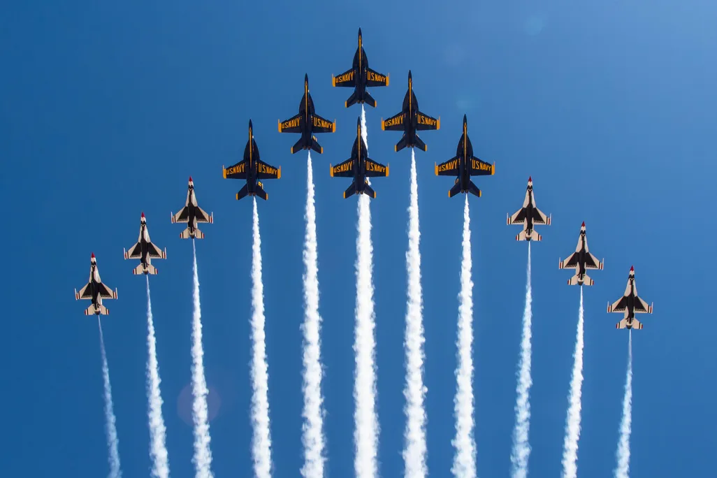 The U.S. Navy Blue Angels and U.S. Air Force Thunderbirds flying in a 12-jet Super Delta formation over the Pensacola Beach Gulf Pier.